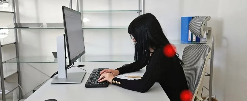 Woman sitting in an ergonomic chair with poor posture, leaning forward at a desk, with highlighted areas indicating neck and lower back pain.