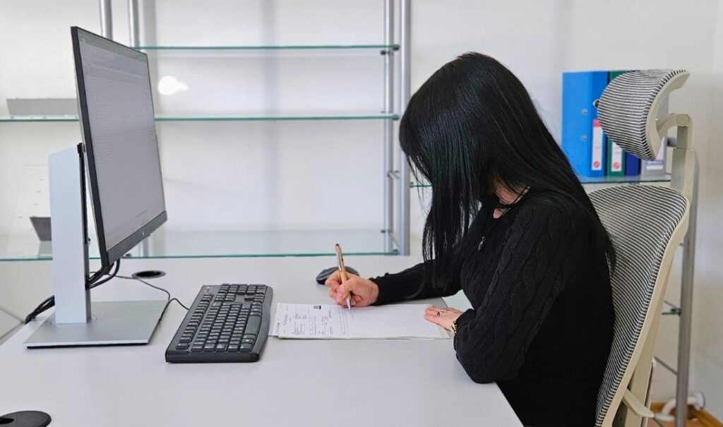 Office worker looking down at documents on the desk, causing forward head posture and increased neck strain during computer work.
